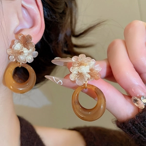 Detail view of resin flower earrings with amber ring pendant on model's ear