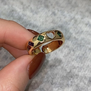 Detailed shot of golden ring with green and purple gemstones and heart-shaped cutouts