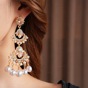 Close-up of fan-shaped tassel earrings with pink crystals and white pearls on a model