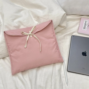 Dettaglio della custodia rosa trapuntata per laptop con fiocco bianco su letto bianco