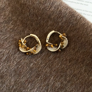 Close-up of golden twisted hoop earrings with brown tiger eye beads on fur background