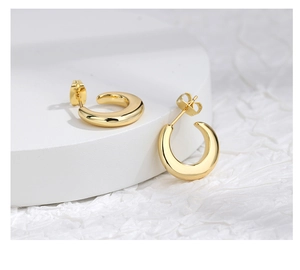 Close-up of polished gold-tone C-shaped hoop earrings on a minimalist display stand