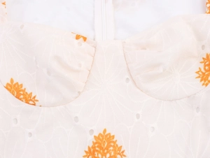 Detalle de bordado inglés floral en vestido blanco roto con flores naranjas