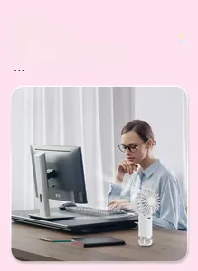 White handheld misting fan with water tank used by a woman at a desk in an office setting