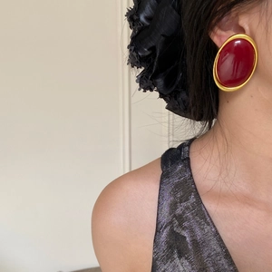 Close-up of vintage oval red stud earring with thick gold frame on female model