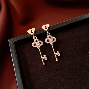 Detail shot of 18k gold plated key pendant earrings with zircon stones on silk