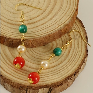 Detail of 18k gold earrings with green malachite, pearl, and red agate beads on wood