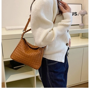 Close-up of brown woven hobo bag with thick braided strap on a model wearing white knitwear