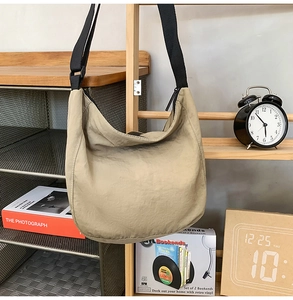 Khaki nylon messenger bag hanging on a wooden rack in a cozy minimalist interior setup