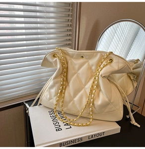 Detail of white quilted tote bag with gold chain straps and sleek faux leather texture
