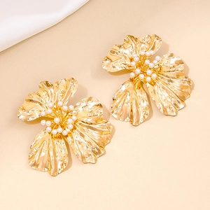 Golden exaggerated metal flower earrings with white pearls on a warm beige background