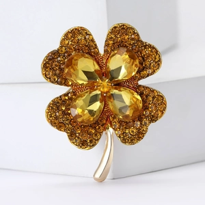 Detail of a gold four-leaf clover brooch featuring amber rhinestones and crystal settings