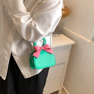 Mini green crossbody bag with pink bow and silver chain, shown on a female model