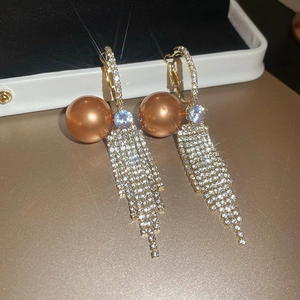 Macro view of gold-plated hoop earrings with brown pearl and shimmering crystal tassels