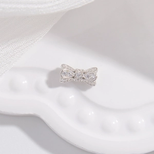 Macro shot of silver bow bead with sparkling cubic zirconia on a white ceramic plate