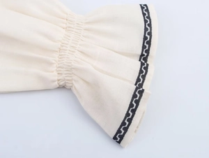 Detailed view of elastic cuffs with black geometric embroidery on white fabric