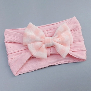 Detail of pink ribbed knit baby headband featuring a large floral checkered bow decoration