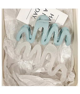 Close-up of wavy resin hair claws in light blue and cream colors on a stylish tray