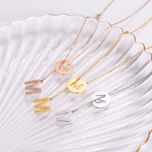 Detailed view of layered letter M pendants in rose gold, gold, and silver finishes