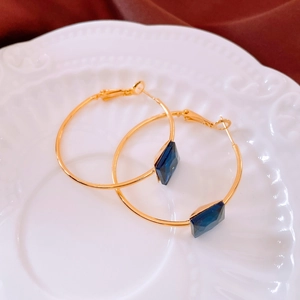 Detail view of 24k gold-plated hoop earrings with square dark blue gemstone on a plate