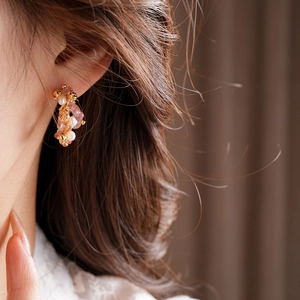Close-up of gold-plated earrings with strawberry crystal, white pearl and flower detail