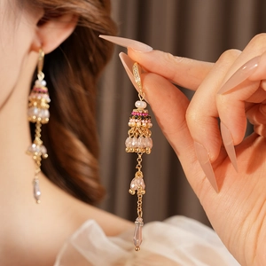 Détail de boucles d'oreilles bohèmes avec perles, pompons et pendentifs gouttes roses