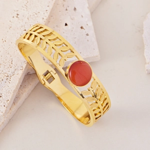 Detail showing leaf镂空 pattern and red-brown stone on a golden stainless steel bracelet