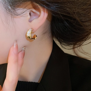 Detailed view of C-shaped gold hoop earring with white enamel and green gemstone accent