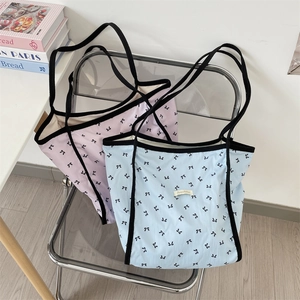Dettaglio di borse tote rosa e blu con motivi a fiocco nero su sedia trasparente
