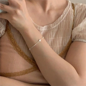 Elegant silver heart pendant bracelet on woman's wrist with soft lace apparel details