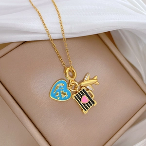 Detail of gold necklace with enamel heart globe, crystal plane, and suitcase charms