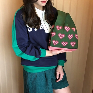 Detail of green knitted tote bag with pink heart pattern held by a model in casual wear