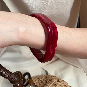 Detail of wide dark red acrylic bangle with marble pattern worn on a woman's wrist