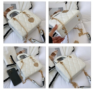 Detail view of a white quilted patent leather handbag with gold chain and heart charm