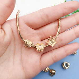 Golden snake chain bracelet featuring shell, butterfly, and crown charms held in hand
