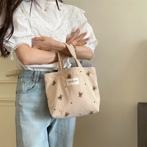 Close-up of beige corduroy tote bag with bear embroidery held by a model in casual wear