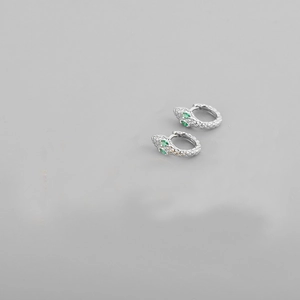 Macro view of silver snake earrings with detailed metal scales and green gemstone eyes