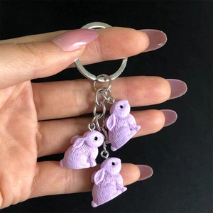 Detailed view of hand holding three lavender resin bunny pendants on a silver keychain ring