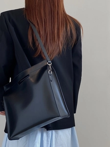 Detail of black leather laptop tote bag with adjustable strap and top handle on model