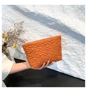 Close-up of caramel orange quilted handbag with 3D floral texture held by hand