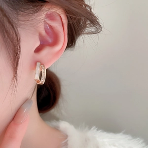 Close-up of gold-plated C-shaped earrings with white shell and shimmering zircons