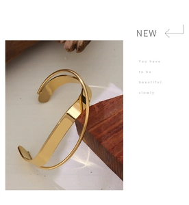 Close-up of a minimalist cross-over golden bangle on dark wood with 18K gold finish