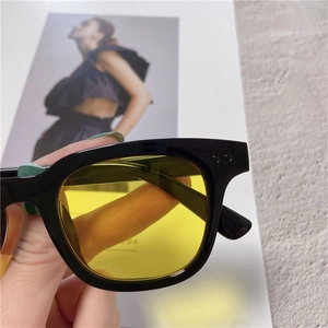 Detail of square black sunglasses with yellow lenses and silver rivet accents