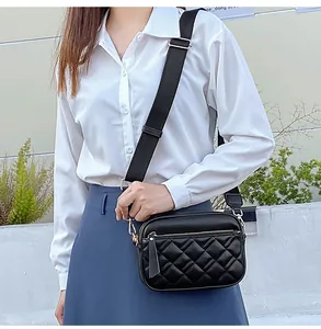 Detail of black quilted crossbody bag showing wide strap and dual zippers on textured leather
