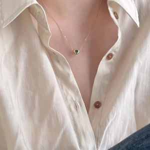 Close-up of minimalist gold heart necklace with a green gemstone worn by a model