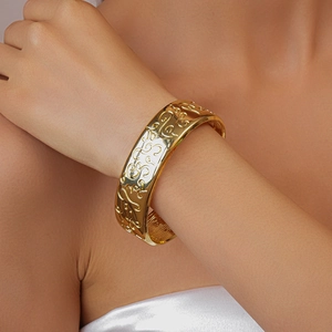 Close-up of golden wide open cuff bracelet featuring detailed vintage floral carvings
