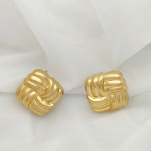 Detail of golden square stud earrings with intricate woven texture on white fabric