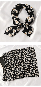 Détail d'un foulard en soie noir imprimé marguerites noué en nœud et posé à plat sur tissu