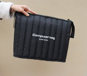 Detail of black quilted laptop sleeve with white Computer Bag text and zipper closure