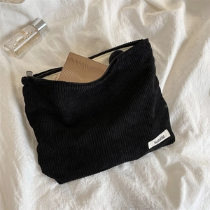 Detail of black corduroy makeup bag with smooth zipper closure and brand logo tag